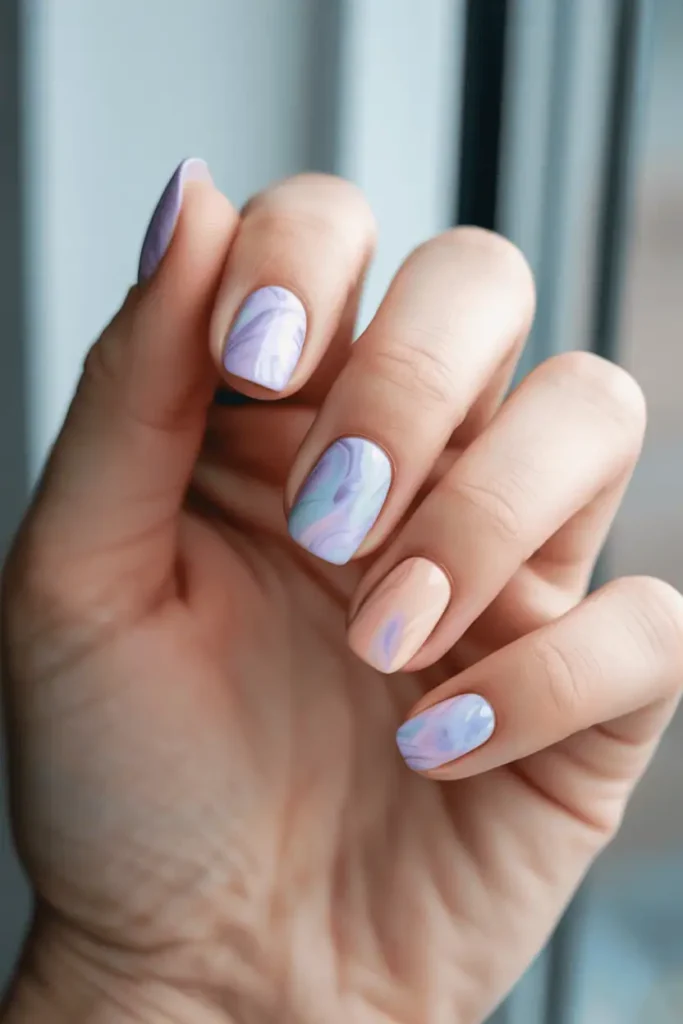 pastel marble nails in lilac, blue, and peach tones, soft watercolor-like texture, realistic hands, bright diffused lighting, gentle minimal spring background