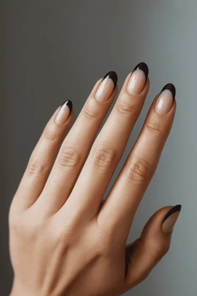 reverse french manicure with black polish at the base of each nail, sheer upper section, modern graphic contrast, realistic hands, minimal background