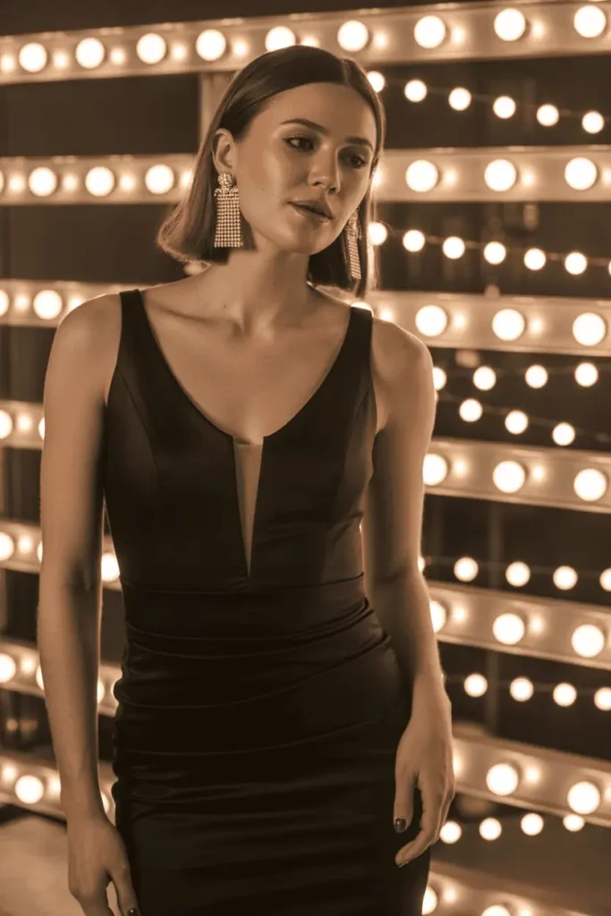 Woman wearing a black cocktail dress with bold earrings under festive lighting.