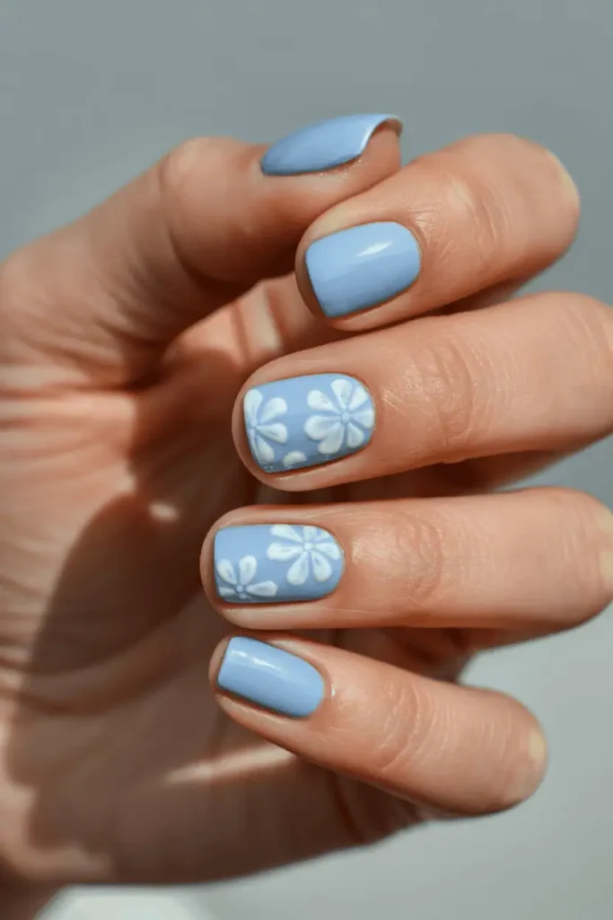 baby blue pastel nails with white floral nail art, soft spring manicure, short nails, glossy finish, delicate flowers, natural lighting, neutral background, professional nail photography, pinterest vertical 2:3 ratio, no text