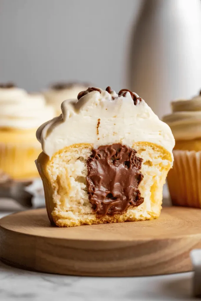 “cupcake cut in half showing chocolate filling inside, soft crumb, light frosting on top, cozy homemade vibe, natural daylight, photorealistic food photography, no text, vertical 2:3”