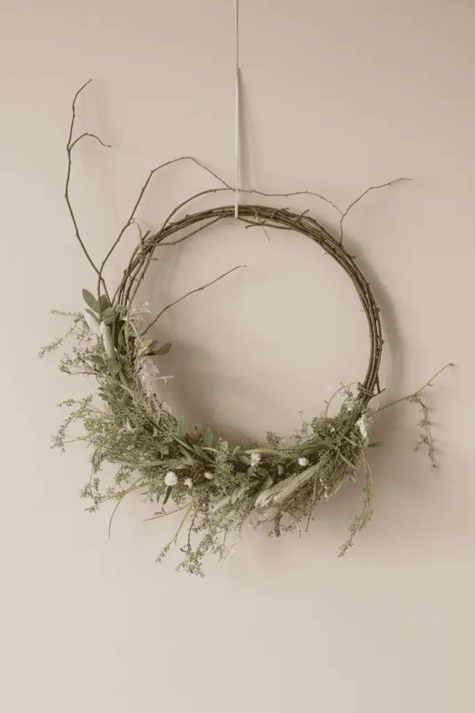 “minimal early spring wreath made with greenery and twigs on a wire hoop, neutral wall background, lots of negative space, calm modern handmade look, soft daylight, realistic photography, no text, 2:3 vertical”
