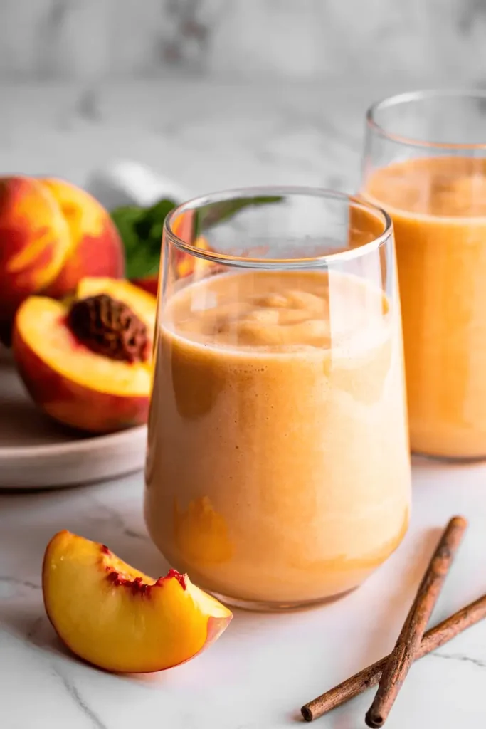 “peach vanilla smoothie in glass, pale peach color, frozen peach slices nearby, soft natural light, clean calm styling, professional food photography, photorealistic, no text, vertical 2:3”