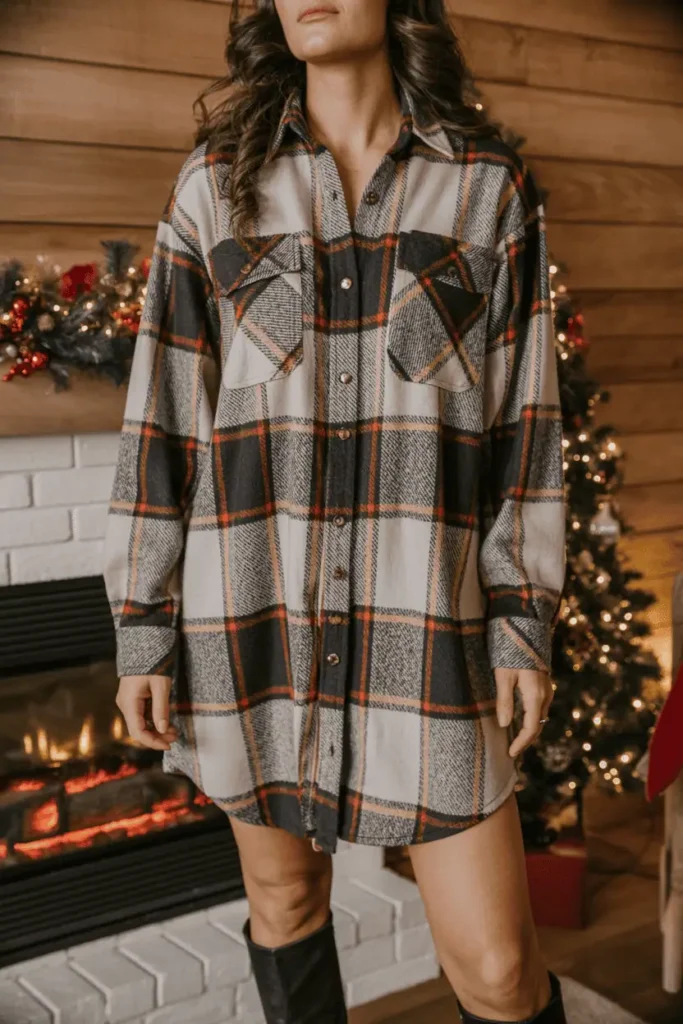 Woman wearing a plaid flannel shirt dress with knee-high boots in a cozy holiday setting.