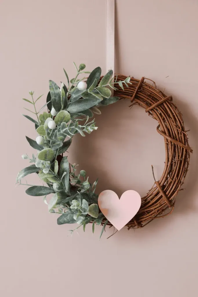 “handmade Valentine’s wreath with faux greenery and small heart accent, partially decorated grapevine wreath, neutral wall background, soft natural light, simple elegant DIY look, realistic photography, no text, 2:3 vertical”