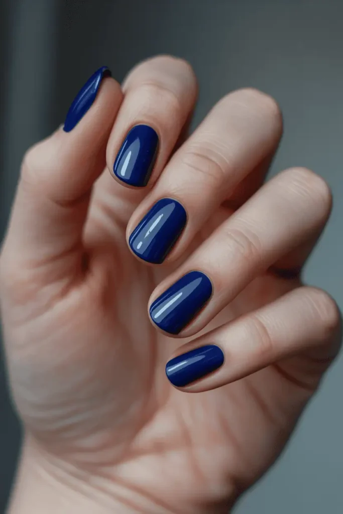 midnight blue glossy nails, rich deep blue shade, subtle shimmer optional, elegant winter lighting, soft moody background, realistic hands