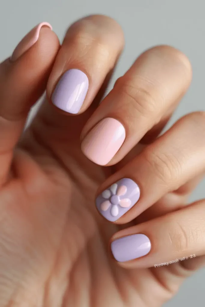 pastel spring nails with floral accent nail, soft pink and lavender nails with small flower detail on one nail, glossy finish, clean feminine look, natural lighting, neutral background, professional nail photography, pinterest vertical 2:3, no text