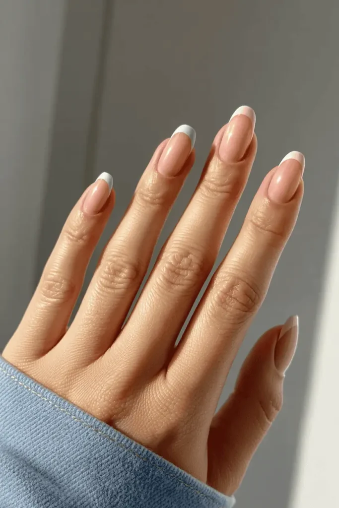 soft blush pink nails with thin pastel French tips, close-up realistic hands, bright natural daylight, minimal chic background, elegant spring vibe